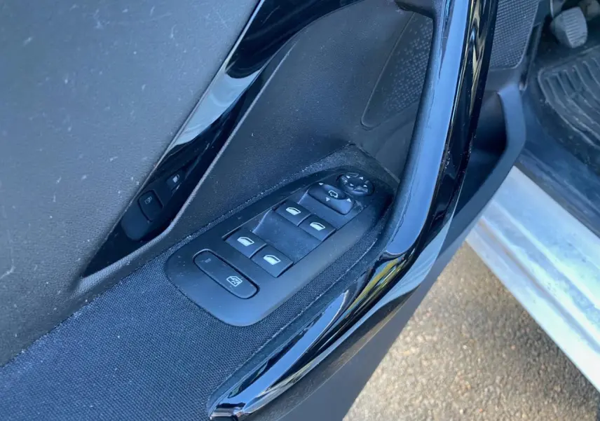 Gros plan sur les commandes des lève-vitres et réglages des rétroviseurs côté conducteur d'une Peugeot 208 noire.