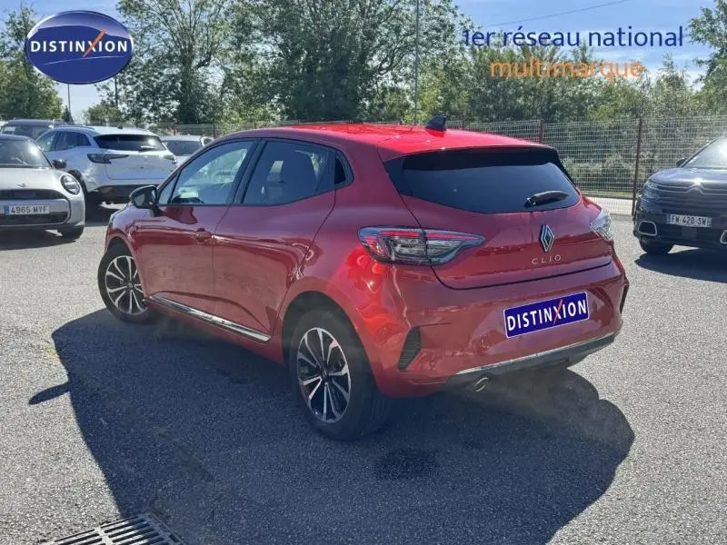 Vue 3/4 arrière droite d'une Renault Clio rouge 2025 avec vitres teintées et jantes alliage noires et argentées.