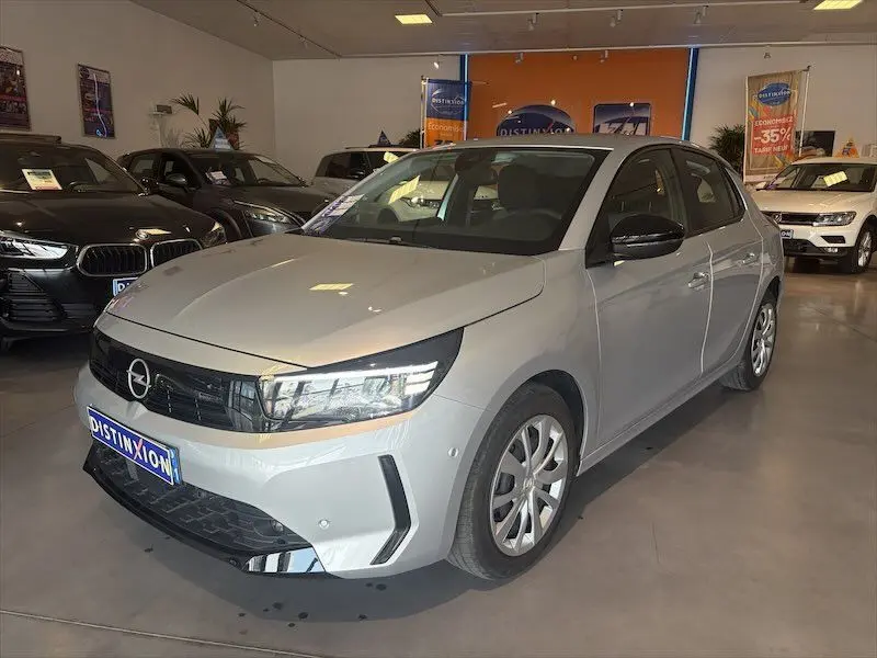 Vue 3/4 avant d'une Opel Corsa gris clair 2025 en concession, avec calandre noire et feux LED distinctifs.