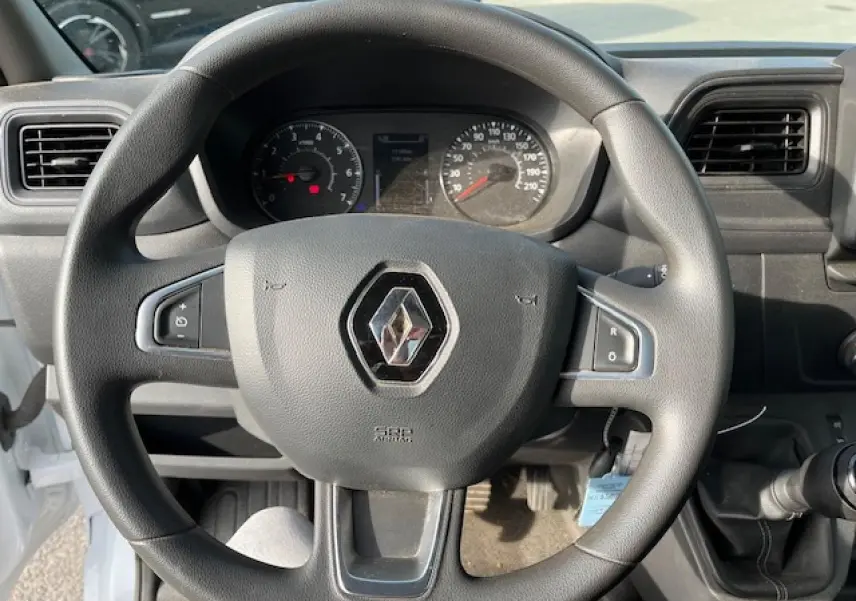 Vue rapprochée du volant noir avec logo Renault du Master 2.3 dCi 130 Benne Basculante blanc, tableau de bord en arrière-plan.