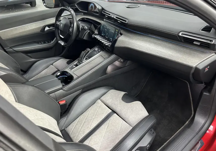 Intérieur avant droit de la Peugeot 508 Hybrid rouge clair, avec sellerie cuir et alcantara gris et tableau de bord moderne.