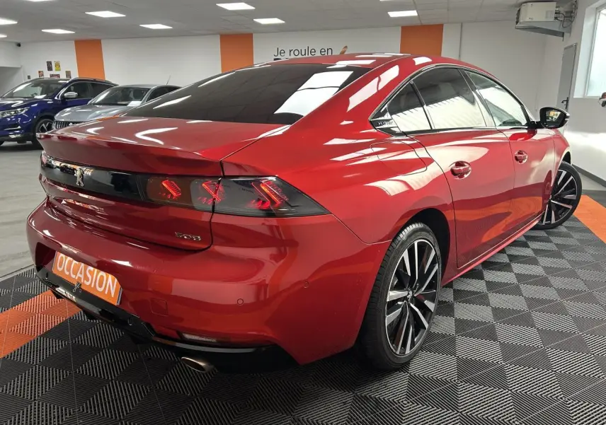 Vue 3/4 arrière droite d'une Peugeot 508 rouge clair avec jantes alliage bi-ton et feux arrière LED distinctifs.