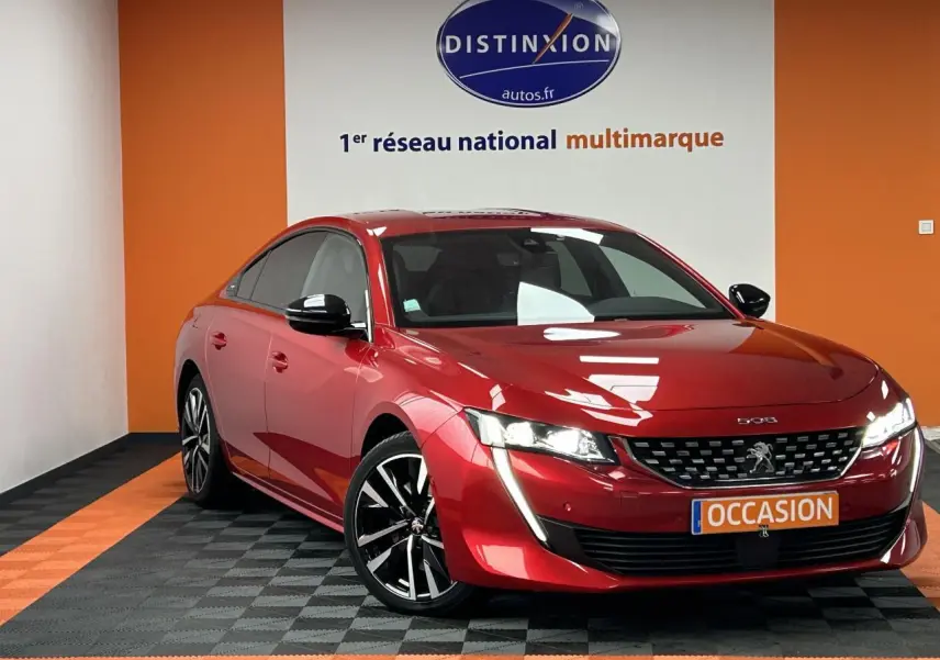 Peugeot 508 rouge clair vue 3/4 avant droit avec jantes alliage et feux LED allumés en showroom.