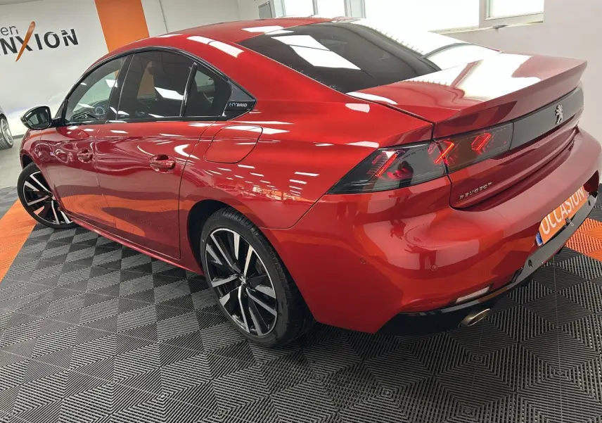 Vue 3/4 arrière droite d'une Peugeot 508 Hybrid rouge clair avec jantes alliage bi-ton et badge Hybrid visible.