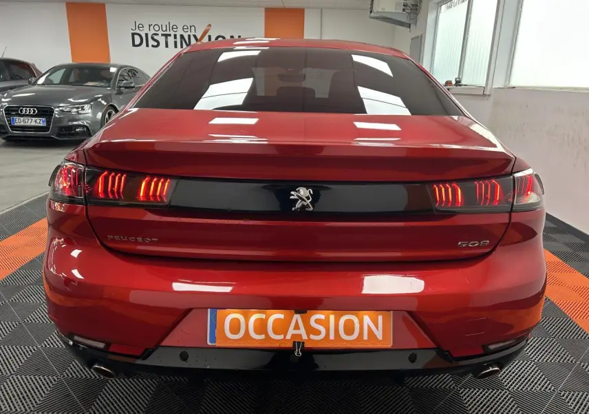 Vue arrière d'une Peugeot 508 rouge clair avec feux LED allumés dans un showroom.