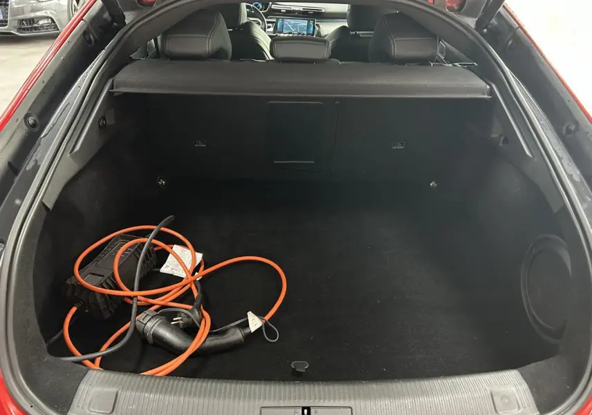 Coffre ouvert d’une Peugeot 508 Hybrid rouge clair avec câble de recharge électrique visible à l’intérieur.