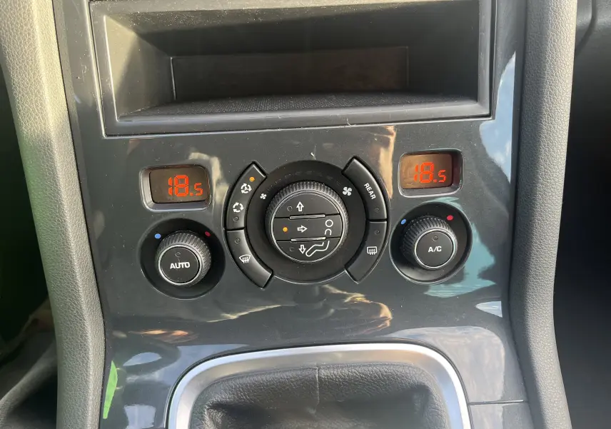 Vue rapprochée de la console centrale noire du Peugeot 5008 2013, avec commandes climatisation et affichage digital rouge.