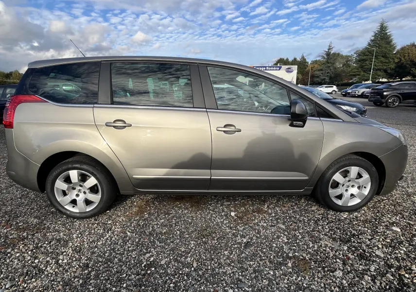 Vue latérale côté gauche d'un Peugeot 5008 gris métallisé de 2013 garé sur un sol gravillonné.