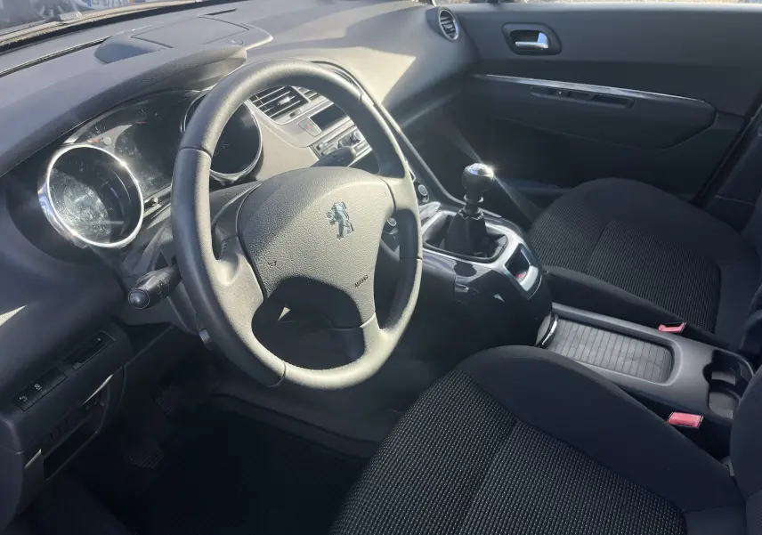 Intérieur noir du Peugeot 5008 2013 vu côté conducteur, volant avec logo lion et levier de vitesse manuel.