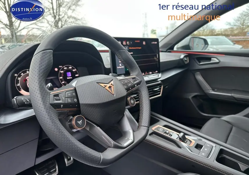 Vue intérieure du poste de conduite du CUPRA LEON ST 1.5 etsi hybrid 2025, volant cuir perforé et écran tactile central.