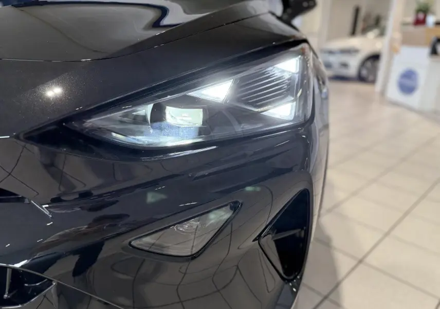 Gros plan sur le phare avant droit allumé d'une CUPRA Formentor 2025 noir Night dans un showroom.