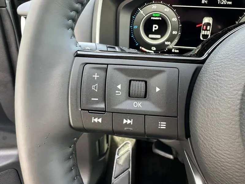 Gros plan sur les commandes au volant à gauche du Nissan Qashqai Hybrid e-POWER 2025, avec tableau de bord numérique en arrière-plan.