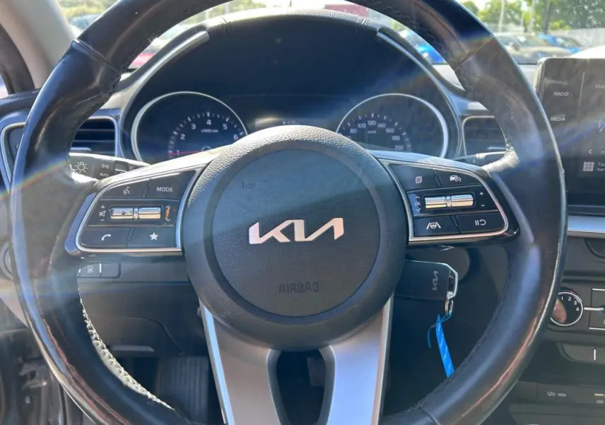 Vue rapprochée du volant noir de la Kia CEE'D 2022 avec commandes intégrées et tableau de bord en arrière-plan.