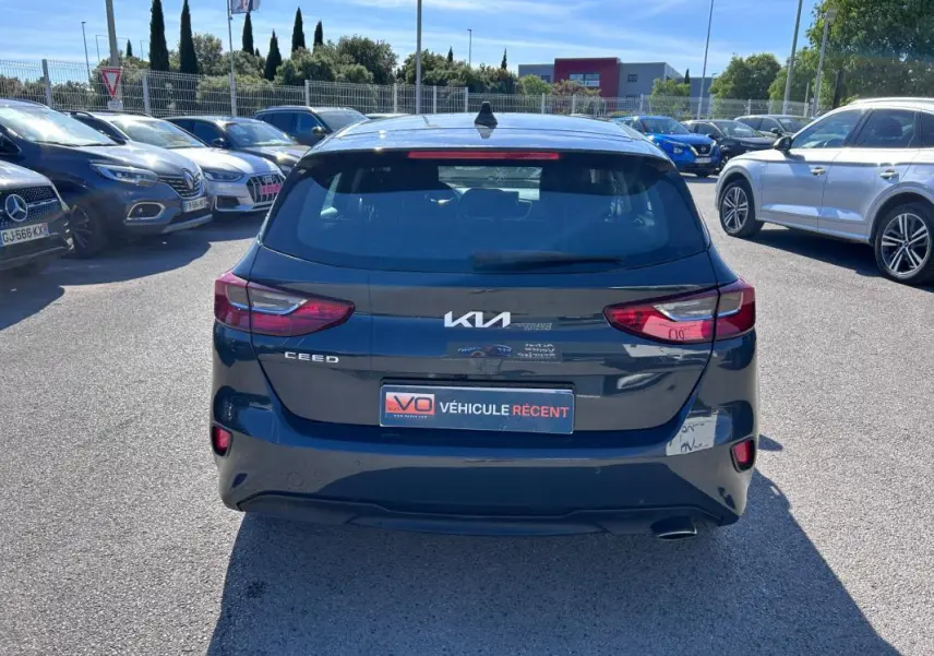 Vue arrière d'une KIA CEE'D gris 2022, avec feux arrière allumés et plaque "Véhicule récent" visible.