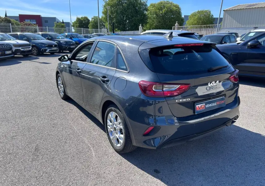 Vue 3/4 arrière droite d'une KIA CEE'D gris métallisé garée en extérieur sur un parking lumineux.