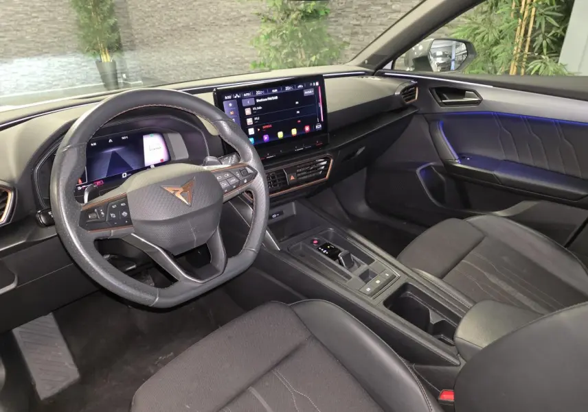 Vue intérieure côté conducteur de la CUPRA Leon 2023, volant cuir noir avec logo Copper et écran tactile central lumineux.