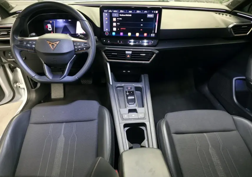 Vue intérieure avant de la CUPRA Leon 2023, volant cuir noir avec logo cuivre et écran tactile central HD.