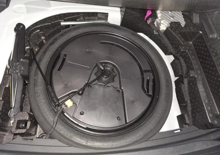 Vue rapprochée de la roue de secours et du cric dans le coffre d’une CUPRA Leon blanche 2023.