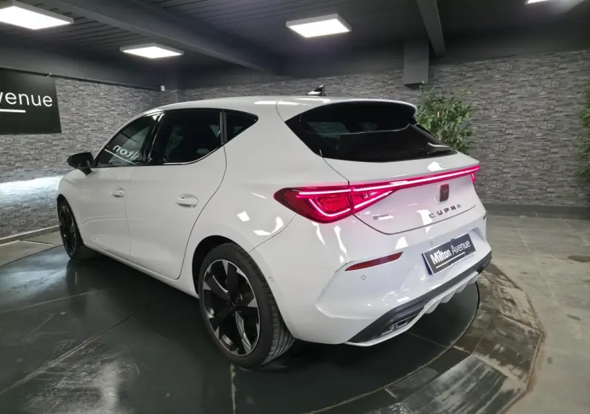 Vue 3/4 arrière droite d'une CUPRA Leon blanche avec feux arrière LED et jantes alliage noires en showroom.
