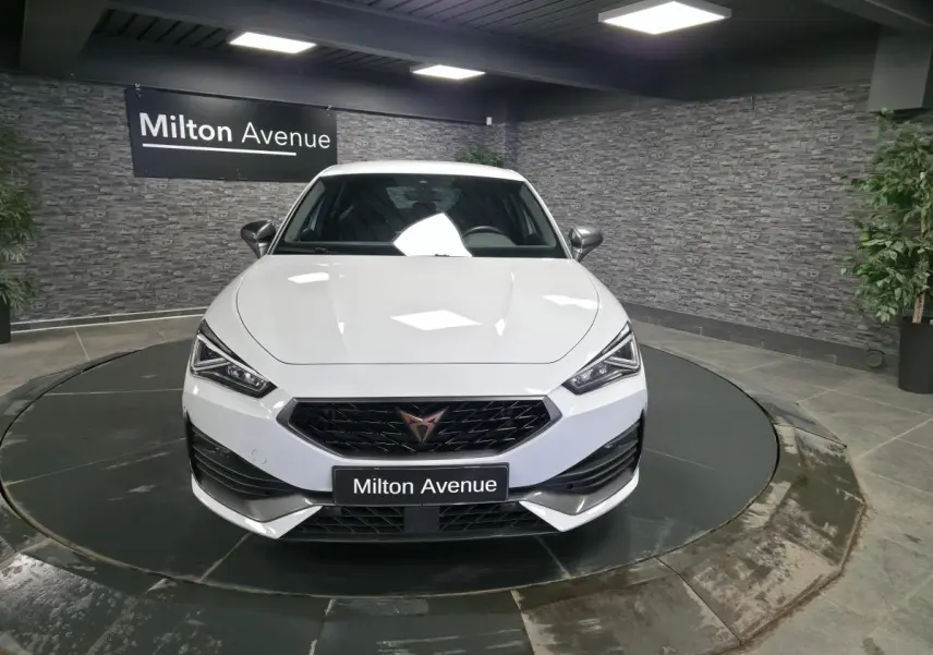 Vue avant d'une CUPRA Leon blanche 2023 avec calandre noire et logo cuivre, sur plateau tournant en showroom.