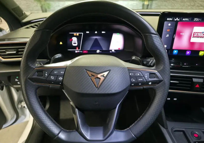 Vue rapprochée du volant Cupra noir avec logo cuivre et tableau de bord digital du Leon 1.5e TSI blanc 2023.