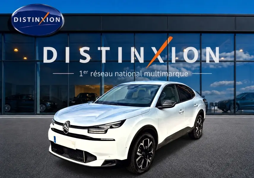 Vue 3/4 avant d'une Citroën C4 X blanche avec jantes alu noires devant une vitrine Distinxion.