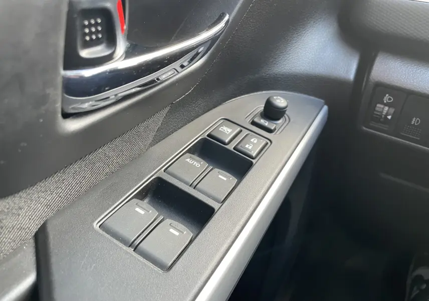 Gros plan sur les commandes des lève-vitres et rétroviseurs côté conducteur d'un Suzuki SX4 S-Cross gris de 2016.