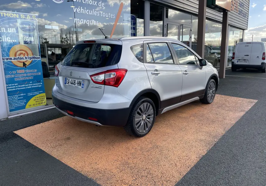 Suzuki SX4 S-Cross gris métallisé vu de trois quarts arrière droit, avec rails de toit et feux arrière distinctifs.