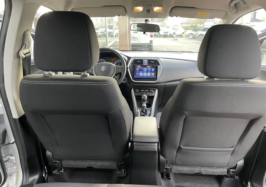 Vue intérieure arrière du Suzuki SX4 S-Cross 2016 gris, montrant sièges avant noirs et console centrale avec écran tactile.