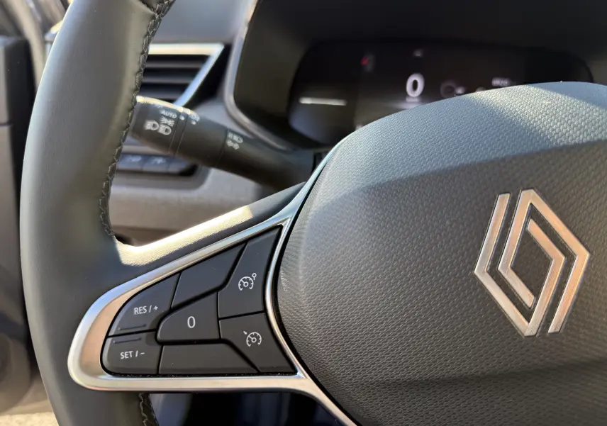 Gros plan sur le volant textile gainé gris de la Renault Clio V avec commandes de régulateur de vitesse intégrées.