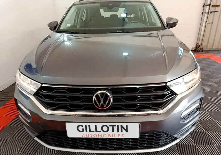Vue frontale d'un Volkswagen T-Roc gris foncé avec calandre noire et logo VW bien visible sur fond intérieur showroom.