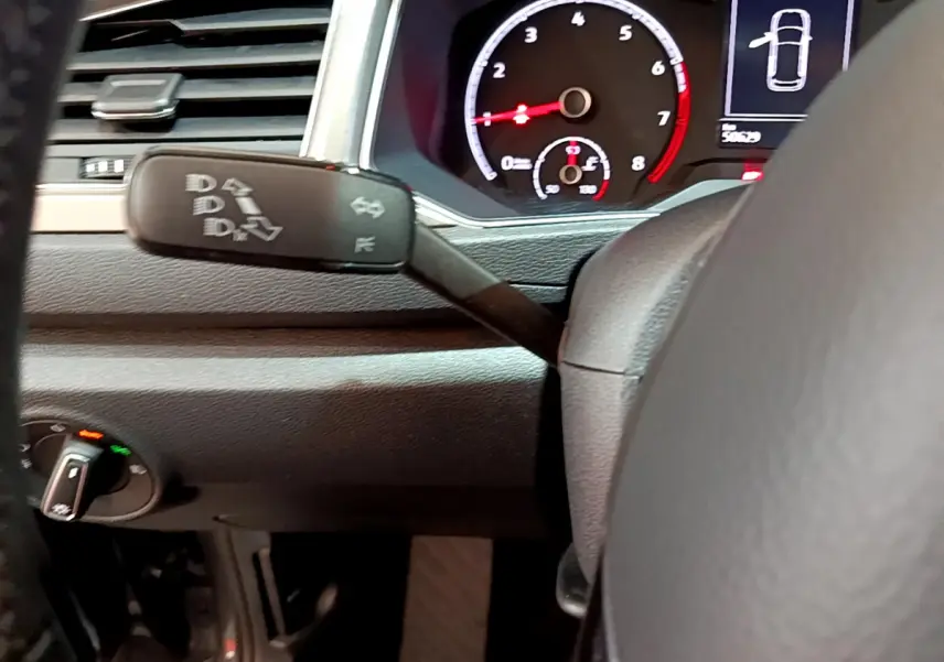 Gros plan sur le tableau de bord et le commodo gauche du Volkswagen T-Roc gris foncé, affichage digital et volant cuir visibles.