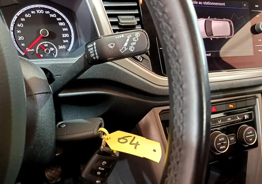 Vue intérieure rapprochée du tableau de bord et volant cuir d’un Volkswagen T-Roc 1.0 TSI 110 Lounge, avec écran tactile et clé insérée.