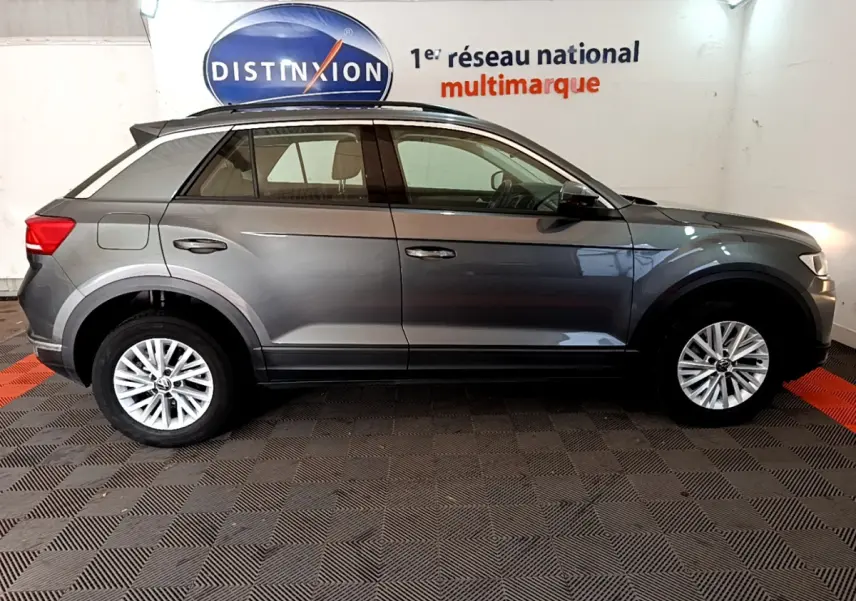 Profil droit d'un Volkswagen T-Roc gris foncé 2021 garé en intérieur avec jantes alliage et barres de toit noires.