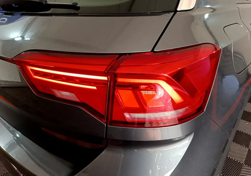Gros plan sur le feu arrière droit rouge du Volkswagen T-Roc gris foncé, avec reflet sur la carrosserie lisse.