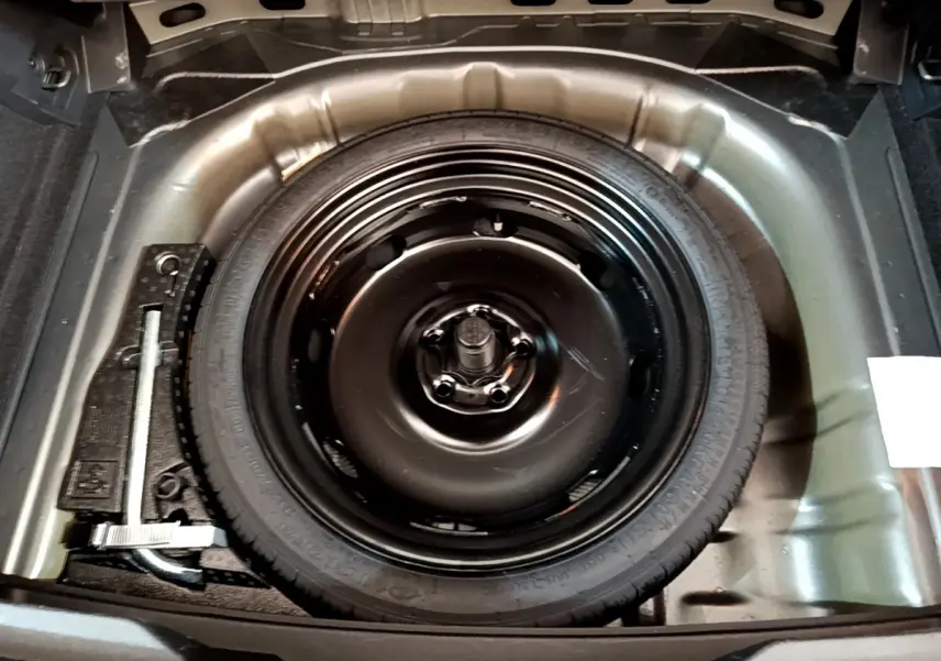 Roue de secours noire dans le coffre du Volkswagen T-Roc gris foncé, vue plongeante sur l'espace de rangement.