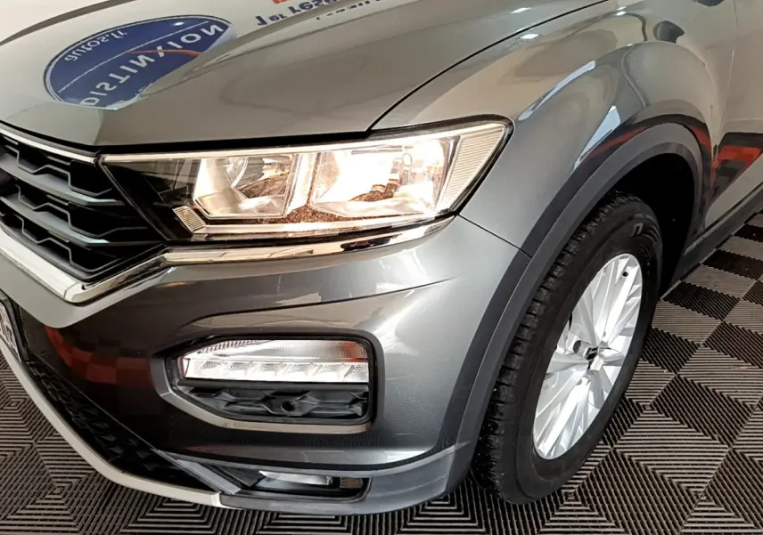 Gros plan sur l'avant droit gris foncé du Volkswagen T-Roc 2021 avec phares allumés et jante alu visible.