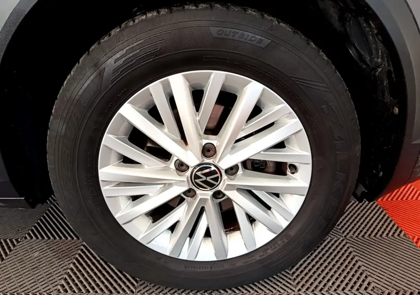 Gros plan sur la jante alliage argentée avec logo Volkswagen du côté avant droit d’un Volkswagen T-Roc gris foncé.