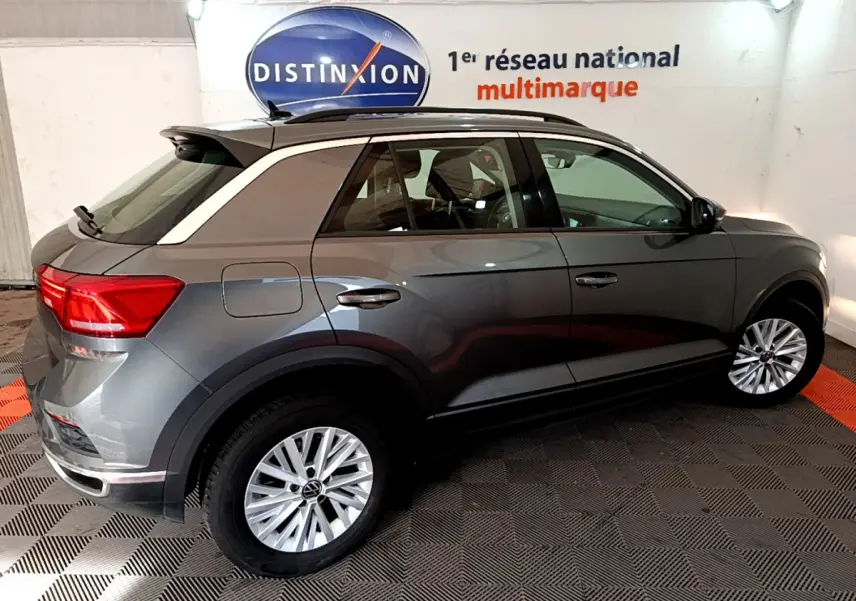 Volkswagen T-Roc gris foncé en vue profil côté gauche, avec jantes alliage et barres de toit noires visibles.