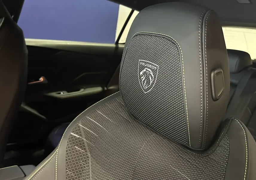 Gros plan sur l'appui-tête avant droit en cuir noir avec logo Peugeot brodé, intérieur sombre de la 308 GT.