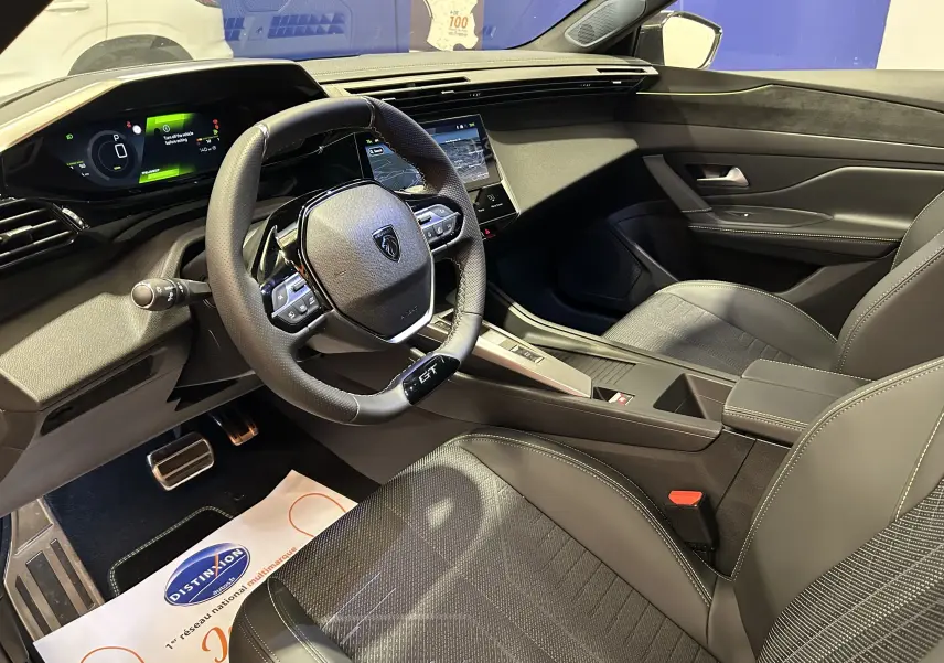 Vue intérieure côté conducteur de la Peugeot 308 GT avec volant compact, sellerie noire et tableau de bord numérique.