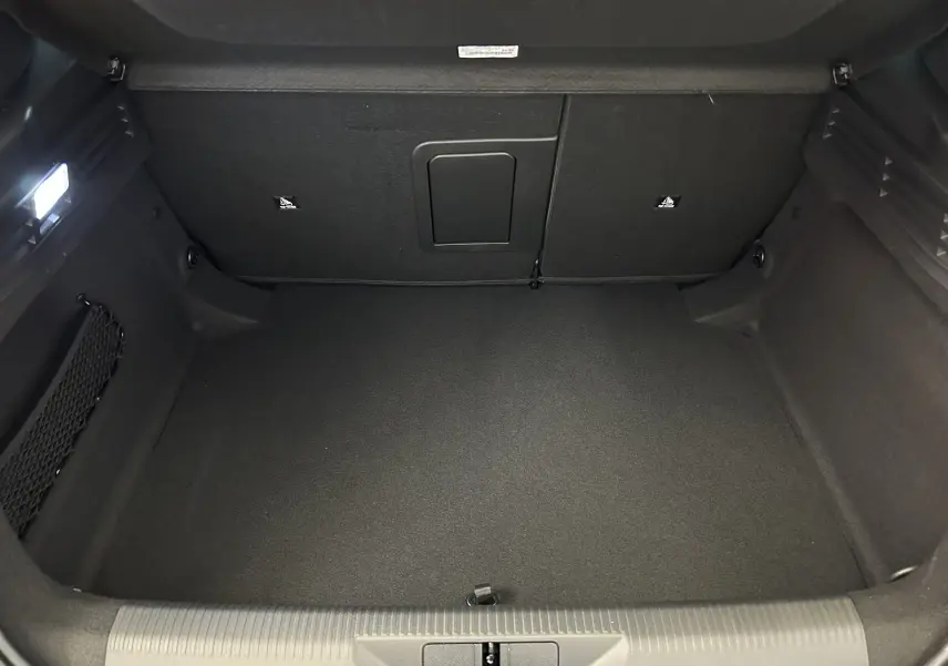 Coffre spacieux de Peugeot 308 gris Artense, vue intérieure arrière montrant un tapis et filet de rangement latéral.
