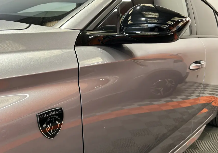 Gros plan sur le côté gauche gris Artense d’une Peugeot 308 III Ph.2 GT avec logo lion et rétroviseur noir brillant.