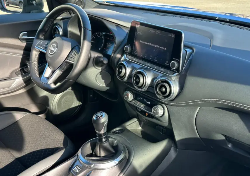 Vue intérieure côté conducteur du Nissan Juke 2023.5 avec tableau de bord noir, écran tactile et levier de vitesses manuel.