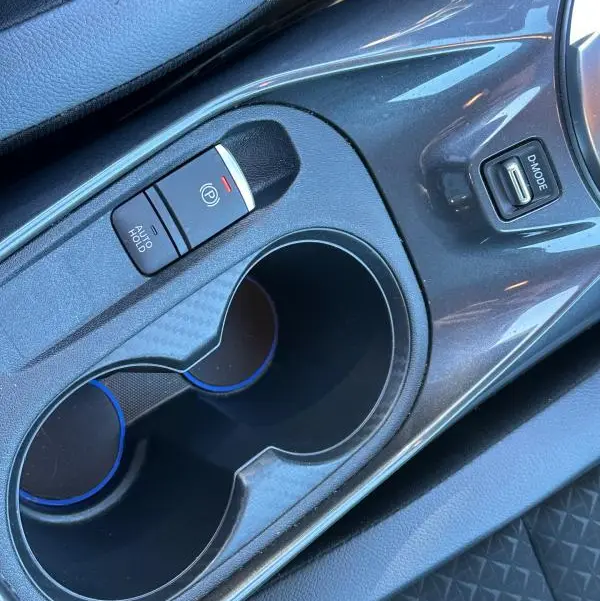 Gros plan sur la console centrale du Nissan Juke 2023.5 bleu clair, montrant le frein à main électrique et porte-gobelets.