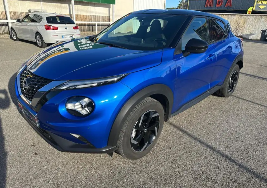 Nissan Juke 2024 bleu clair vu en 3/4 avant droit, avec jantes alliage noires et calandre distinctive V-Motion.