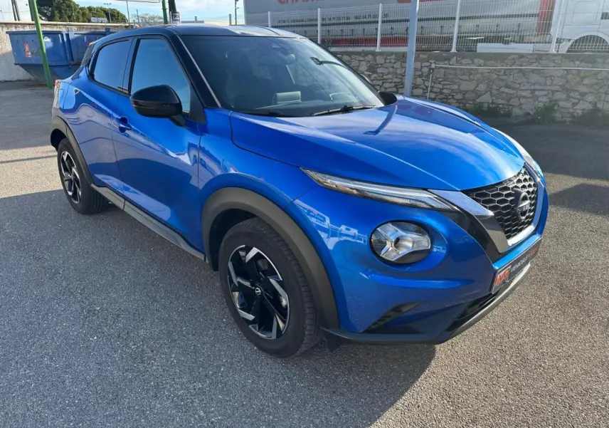 Nissan Juke 2024 bleu clair en 3/4 avant droit, avec jantes alliage noires et calandre en V distinctive.