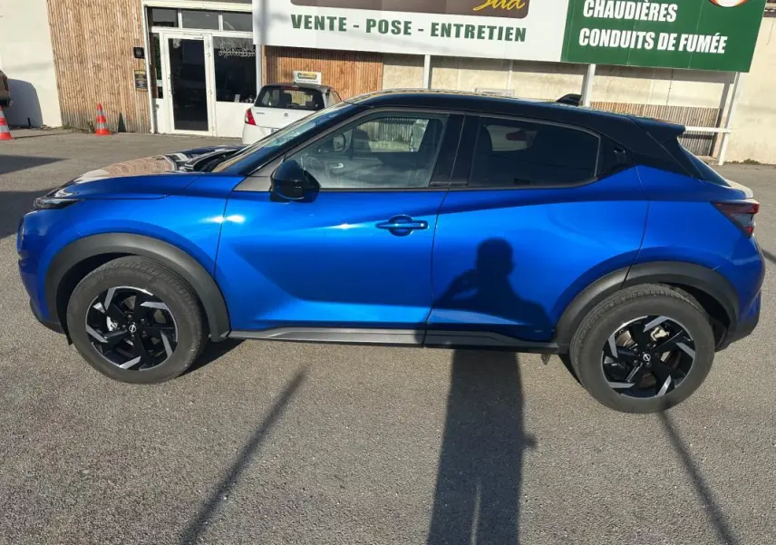Vue de profil côté gauche d'un Nissan Juke 2024 bleu clair avec jantes alliage noires de 17 pouces sur parking.