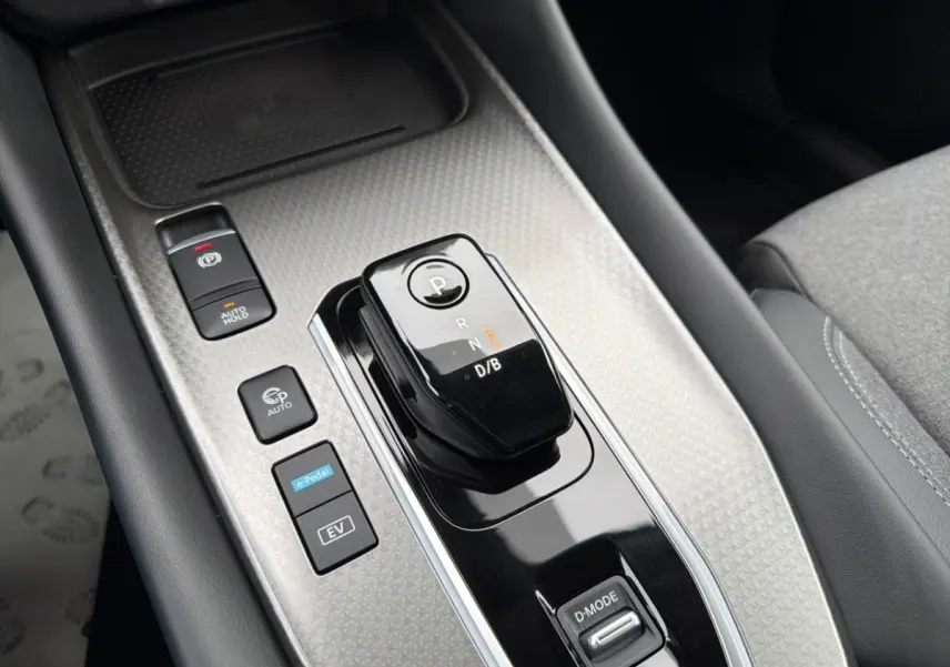 Gros plan sur la console centrale noire et grise du Nissan Qashqai 1.5 e-Power avec levier de vitesses automatique et boutons fonctionnels.