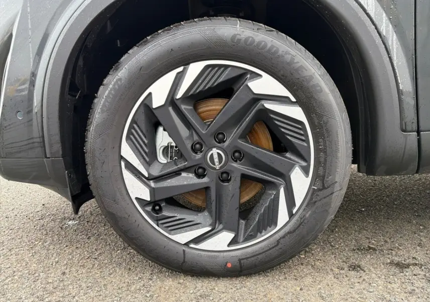 Gros plan sur la roue avant gauche noire du Nissan Qashqai 1.5 e-Power avec jante alu bicolore et logo Nissan central.